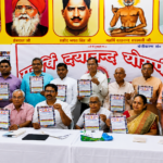 Organizers displaying the official schedule flyer for Arya Virangana and Purohita training camp at Sikandara in Agra review setup