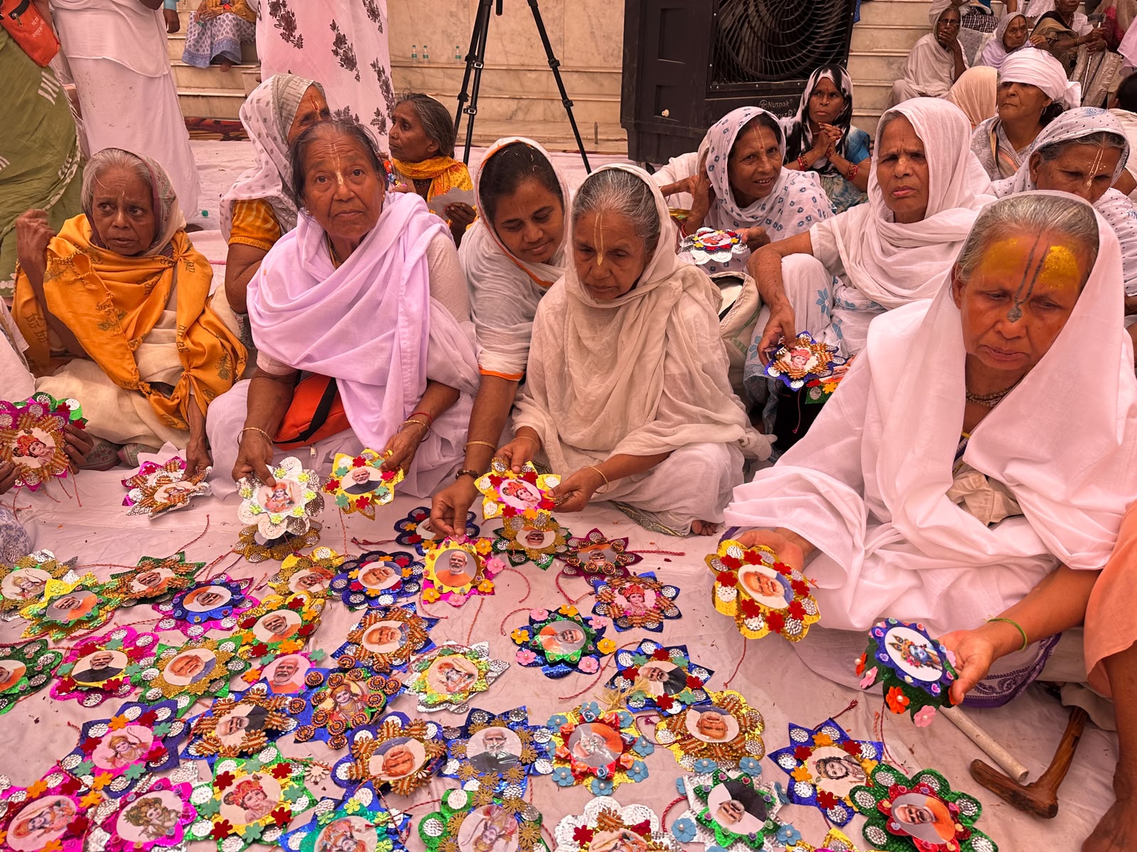 वृंदावन के गोपीनाथ मंदिर में सुलभ इंटरनेशनल की कार्यकारी संयोजिका नित्या पाठक और पीएम मोदी की तस्वीर वाली राखी प्रदर्शित करतीं माताएं